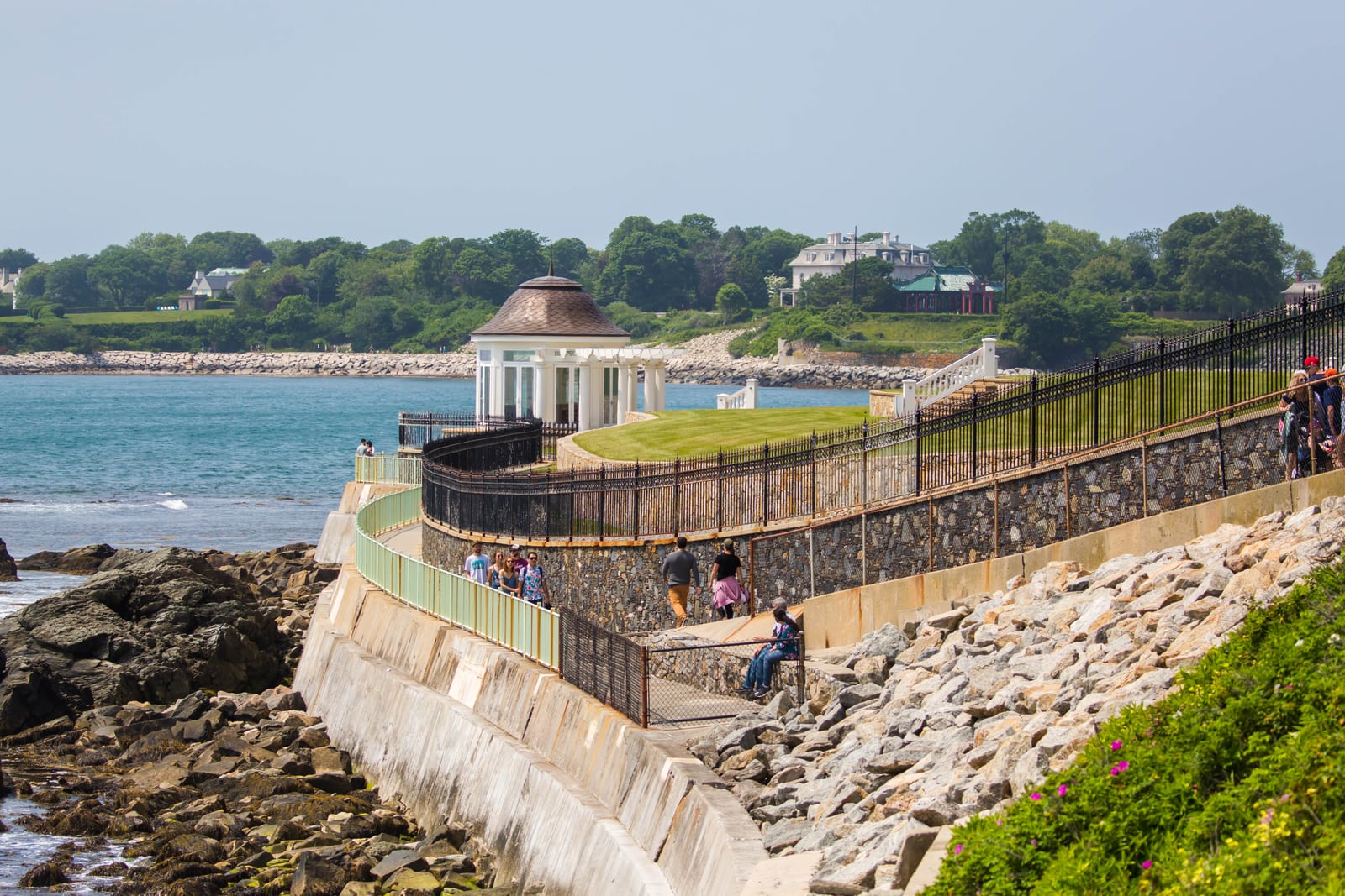 Visitors on Newport Cliff Walk beside a rocky shore and mansion grounds